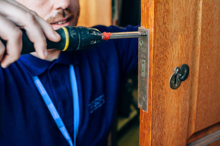 locksmith fixing wooden door with screwdriver